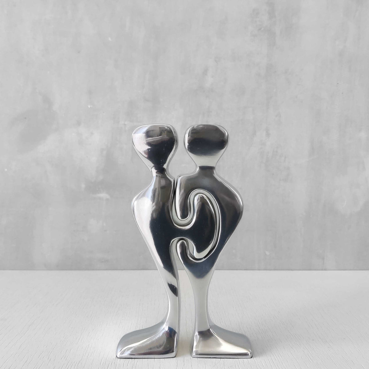 A pair of sculptural cast aluminium figural interlocking candle holders