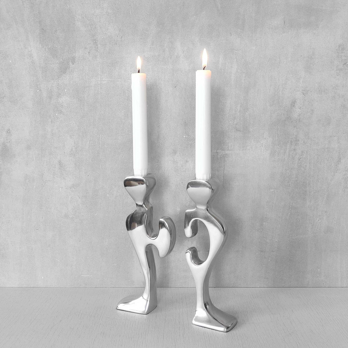 A pair of sculptural cast aluminium figural interlocking candle holders