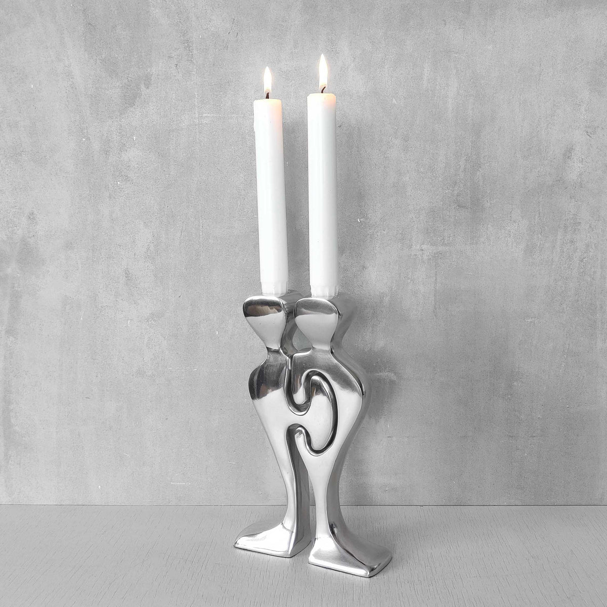 A pair of sculptural cast aluminium figural interlocking candle holders