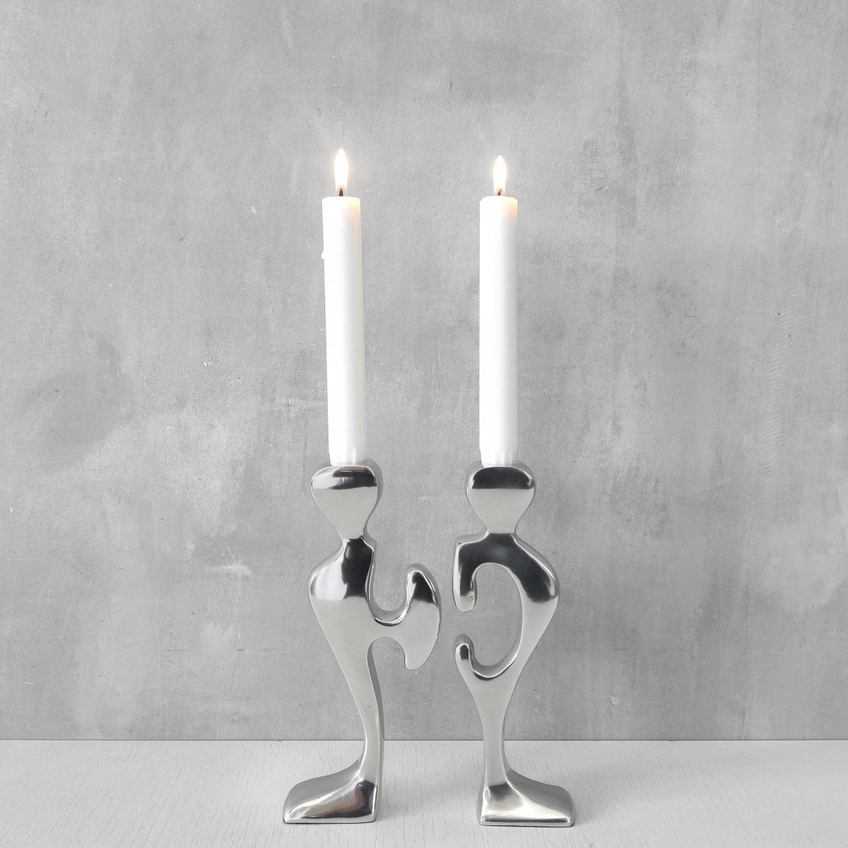 A pair of sculptural cast aluminium figural interlocking candle holders