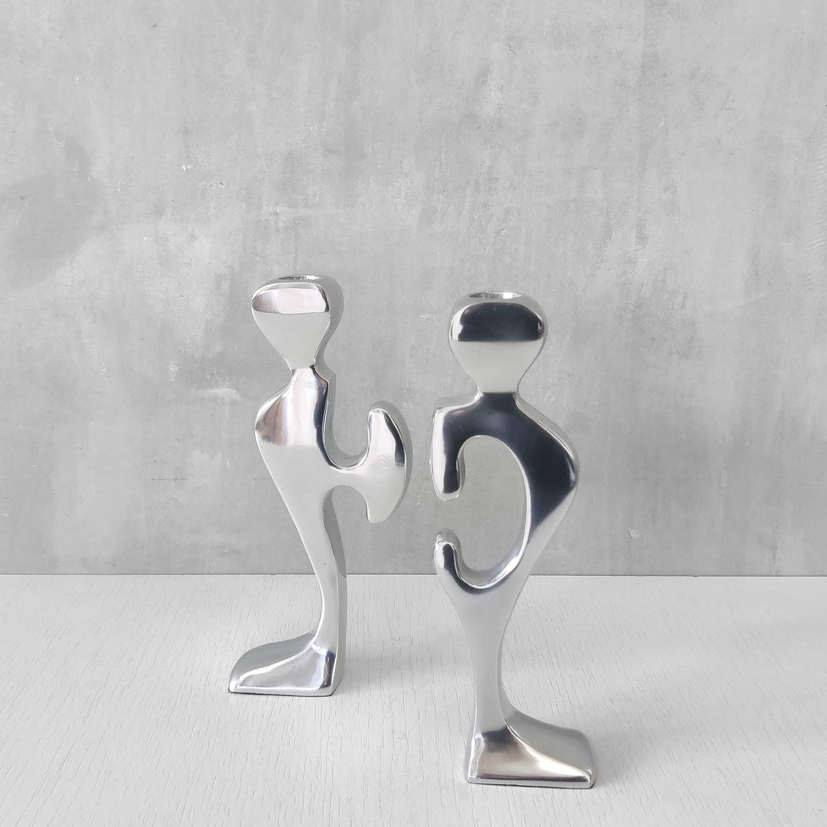 A pair of sculptural cast aluminium figural interlocking candle holders