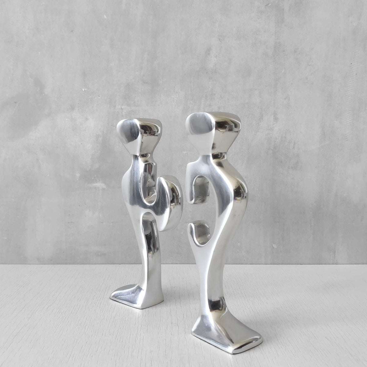 A pair of sculptural cast aluminium figural interlocking candle holders