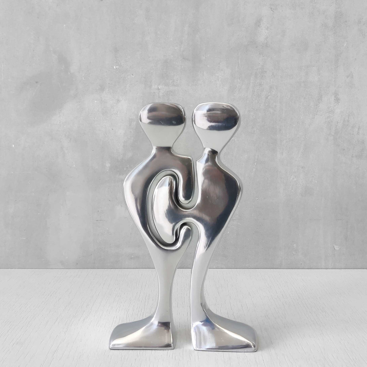 A pair of sculptural cast aluminium figural interlocking candle holders