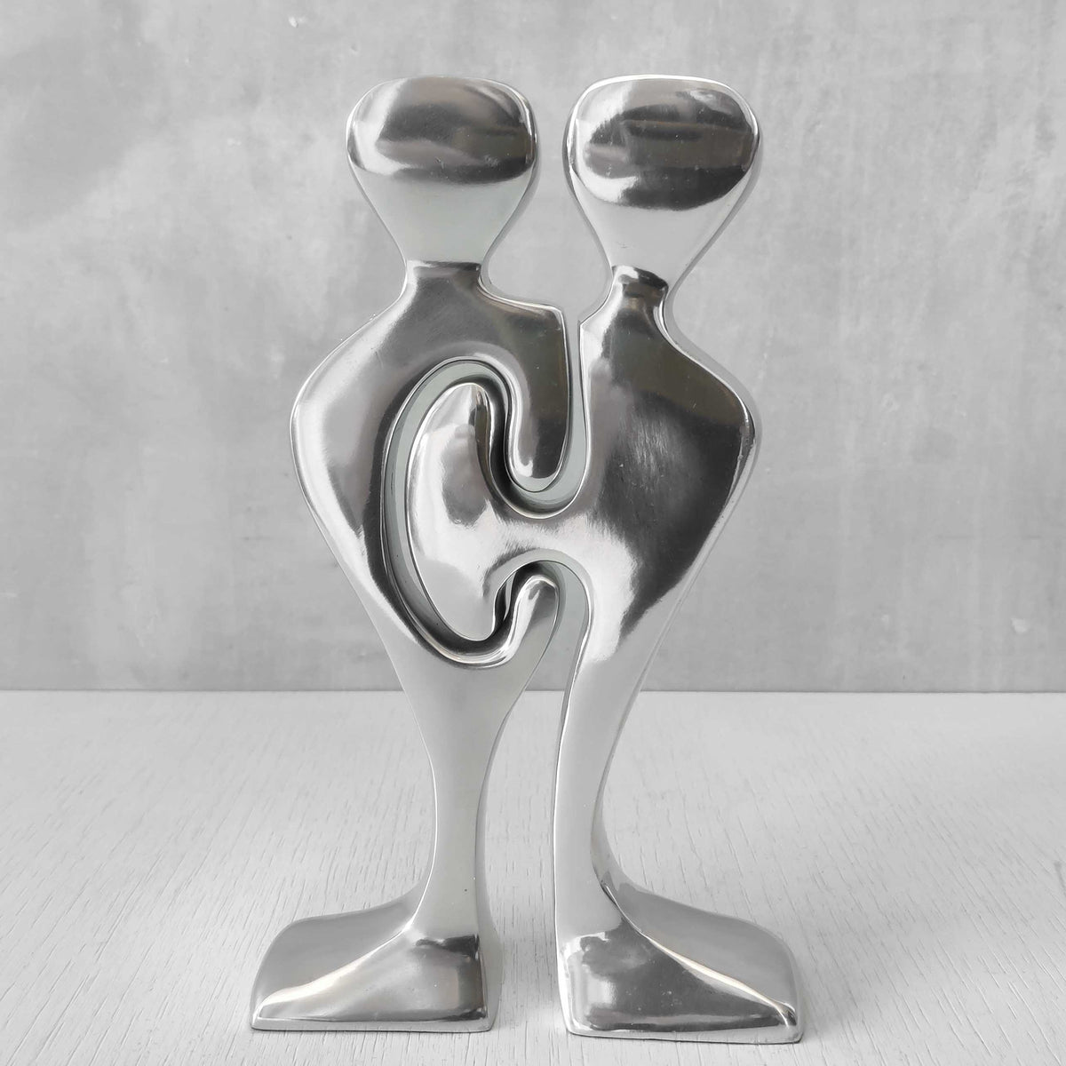 A pair of sculptural cast aluminium figural interlocking candle holders