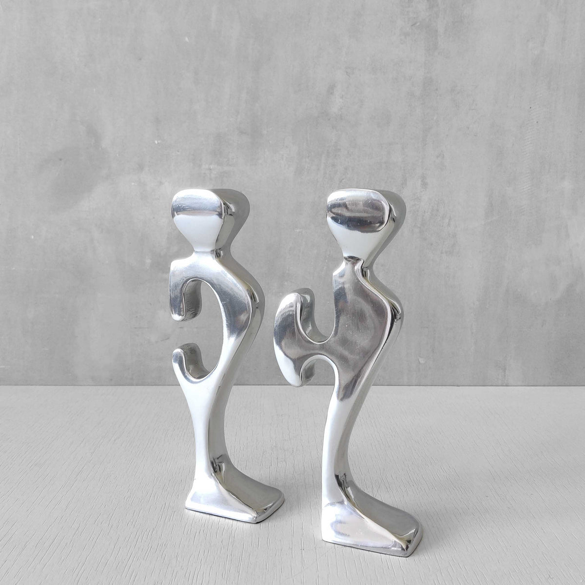 A pair of sculptural cast aluminium figural interlocking candle holders