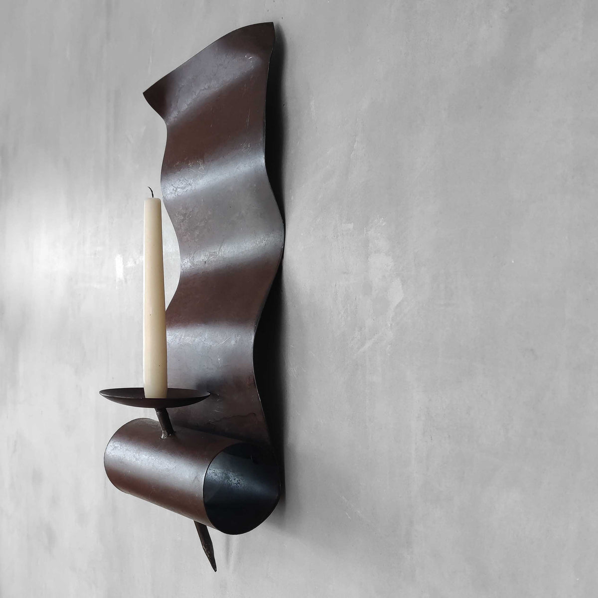 A large steel patinated wavy scrolled sculptural candle sconce