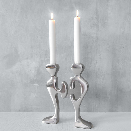 A pair of sculptural cast aluminium figural interlocking candle holders